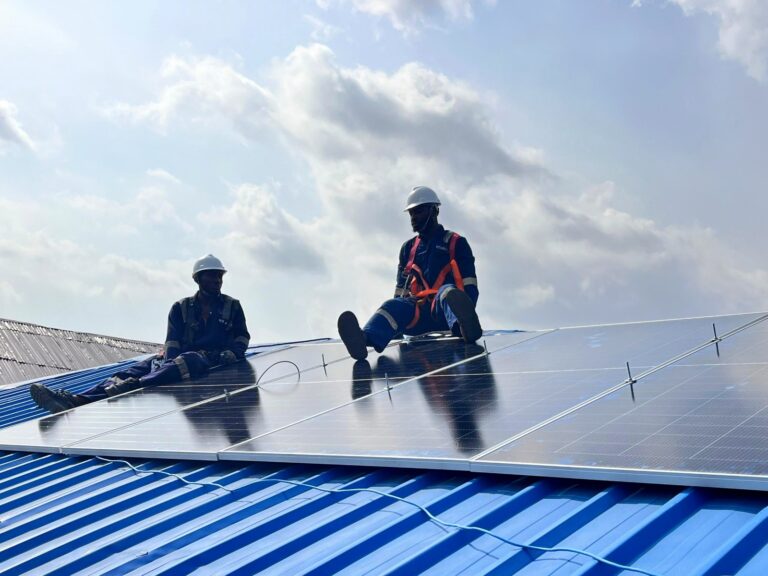 Two technicians installing solar panels on a blue metal roof