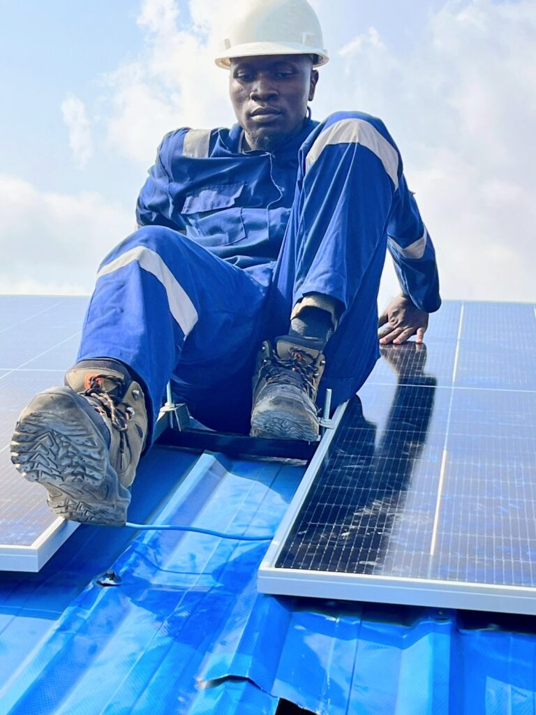 Technician seated beside newly installed solar panels on a metal roof